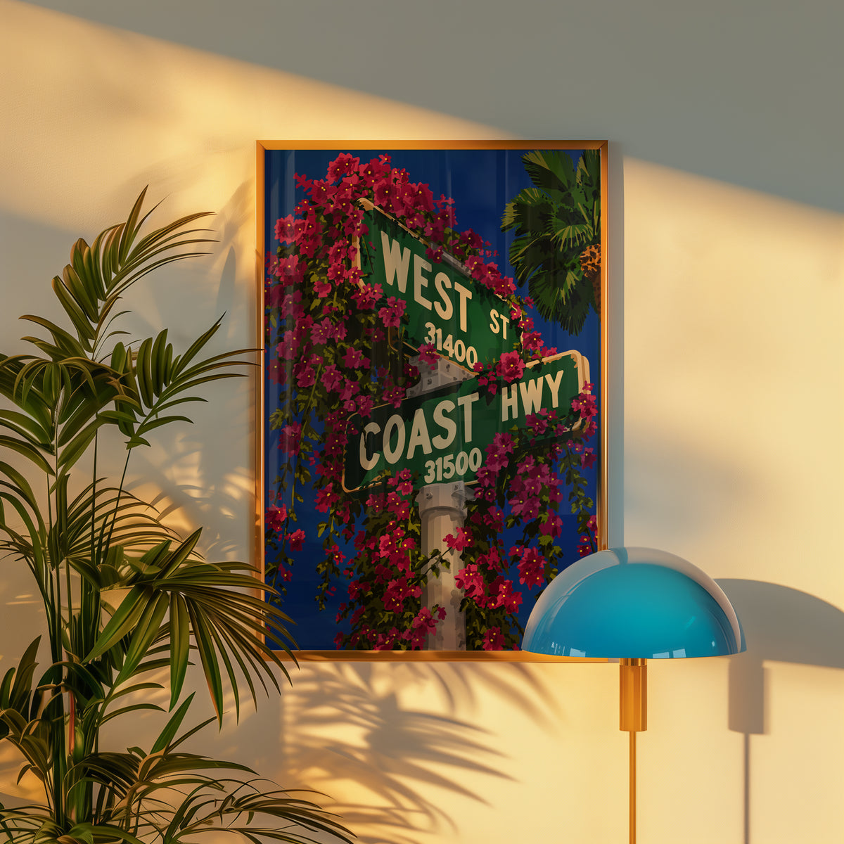 West Coast print in a gold frame on a warm wall beside a palm plant and blue dome lamp