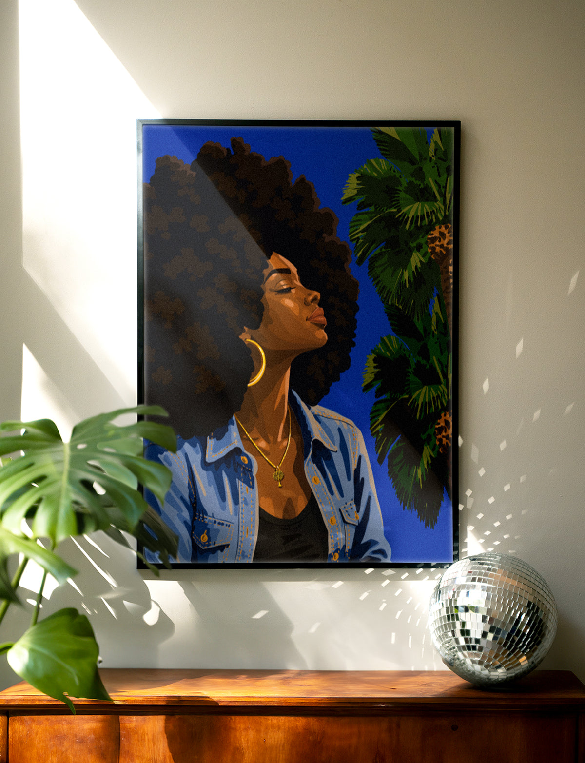 Sun Kissed print framed in black on a wall above a wood dresser with a monstera plant and disco ball